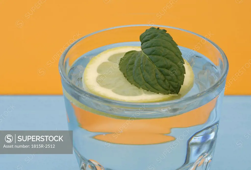 Peppermint leaf on lemon slice in glass of water, close-up