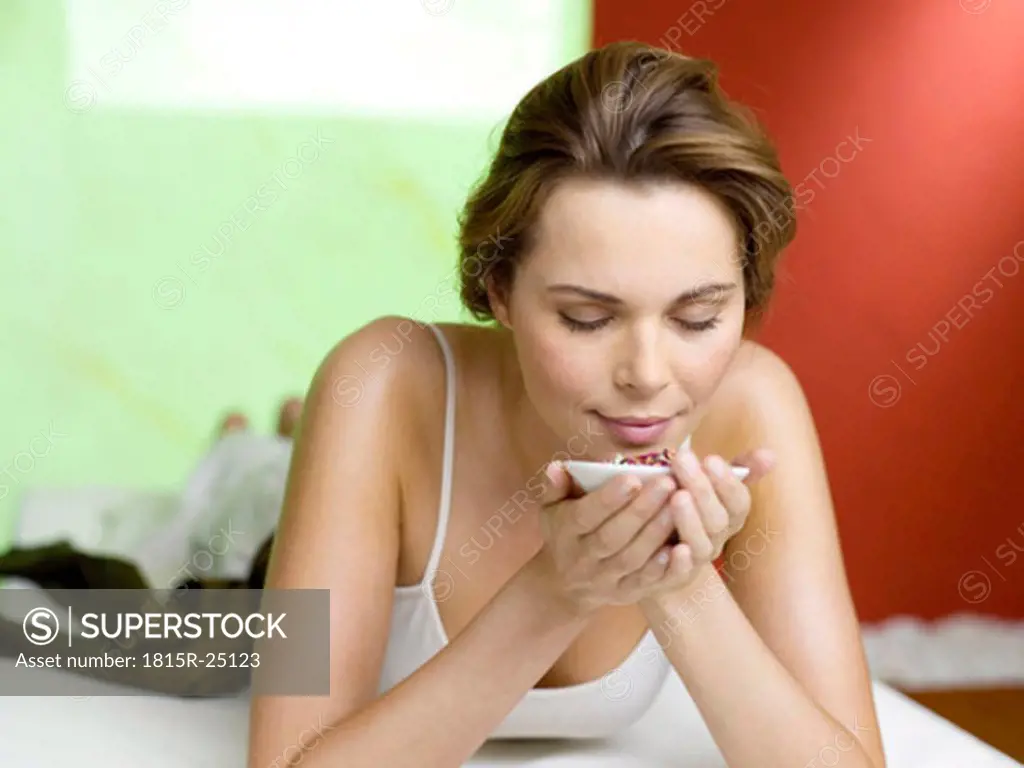 Woman lying on bed smelling spice in bowl, eyes closed