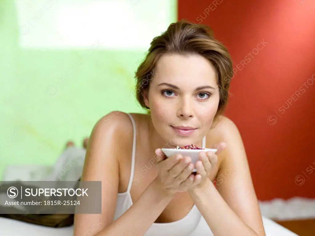 Woman lying on bed, holding spice bowl, portrait