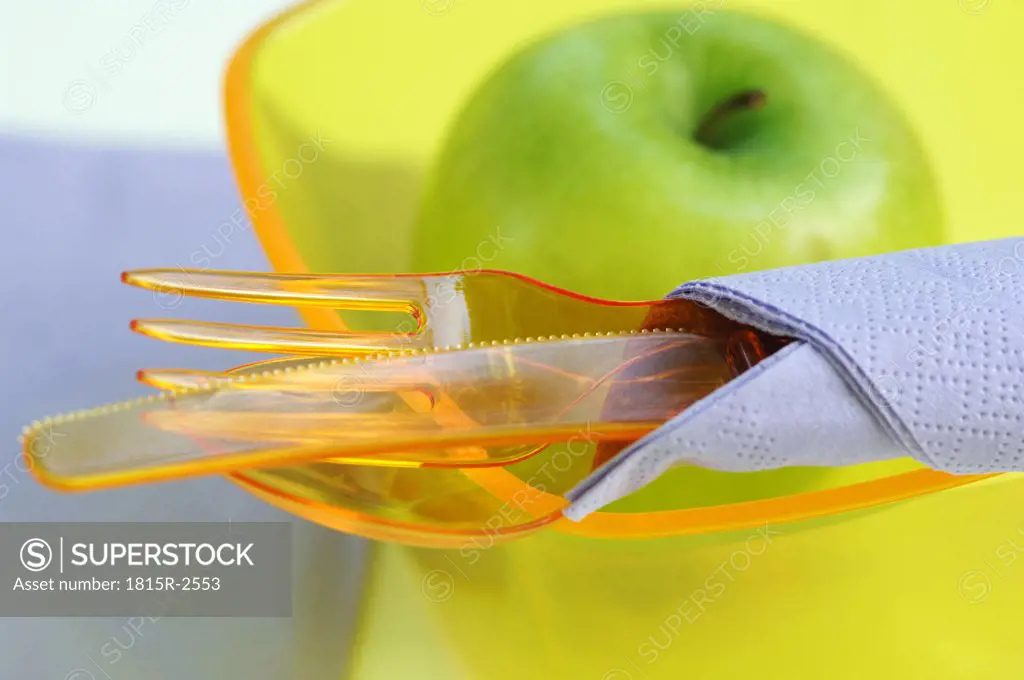 Plastic cutlery, plastic bowl and green apple