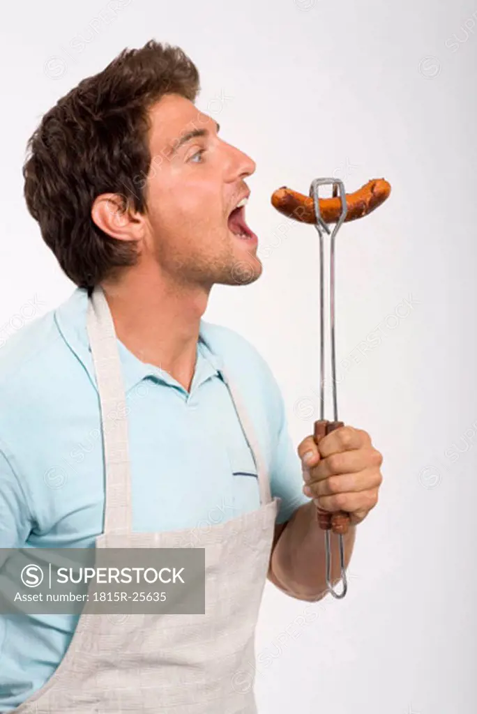 Young man holding grilled sausage, close up