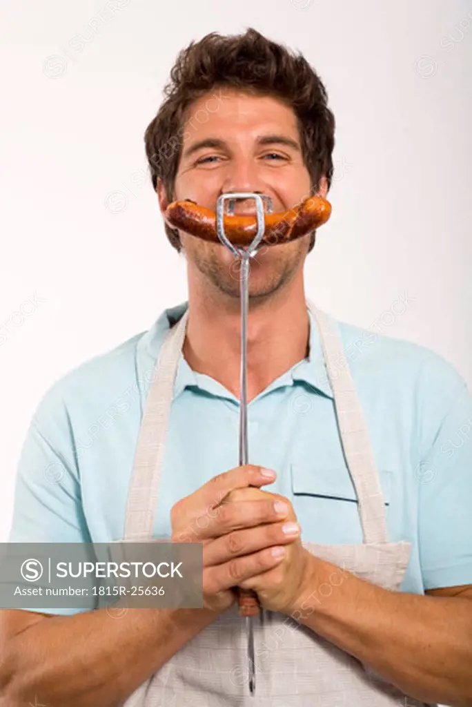 Young man holding grilled sausage, close up, portrait