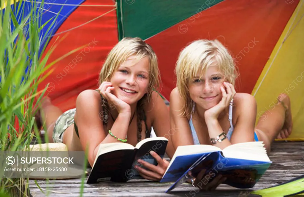 Teenage girls (13-15) lying under sunshade on jetty, reading book, portrait