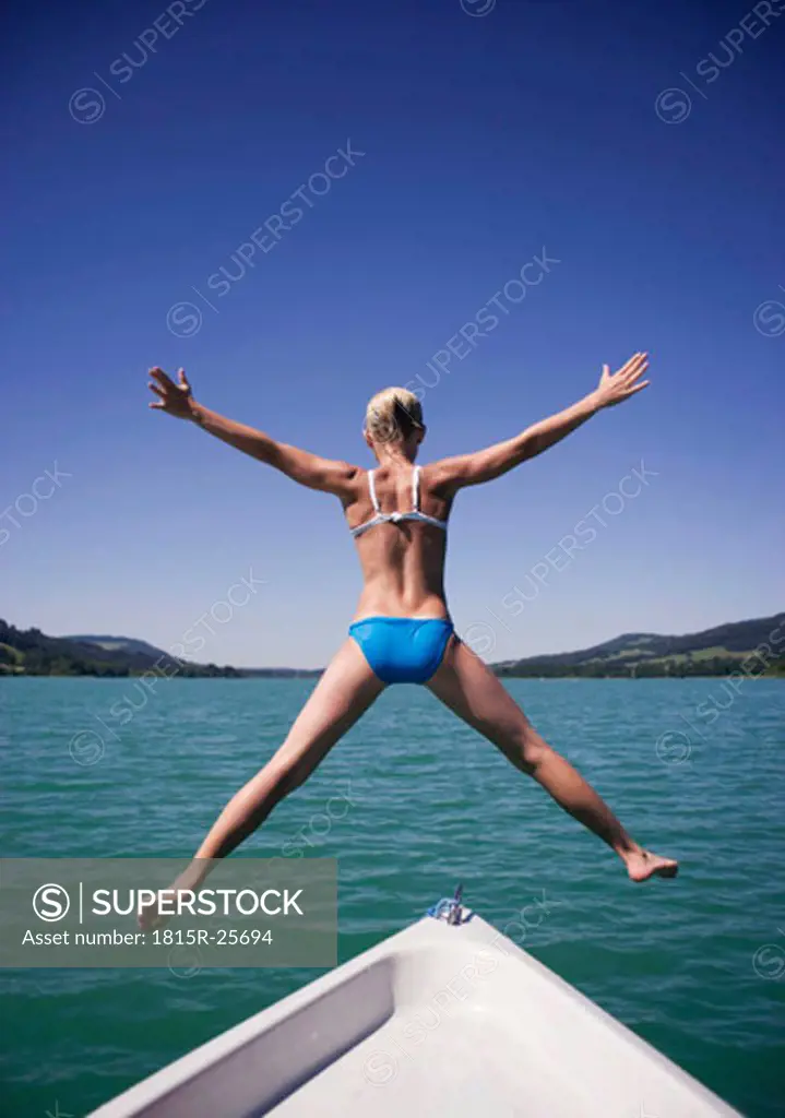 Teenage girl (13-15) jumping from boat into water, rear view