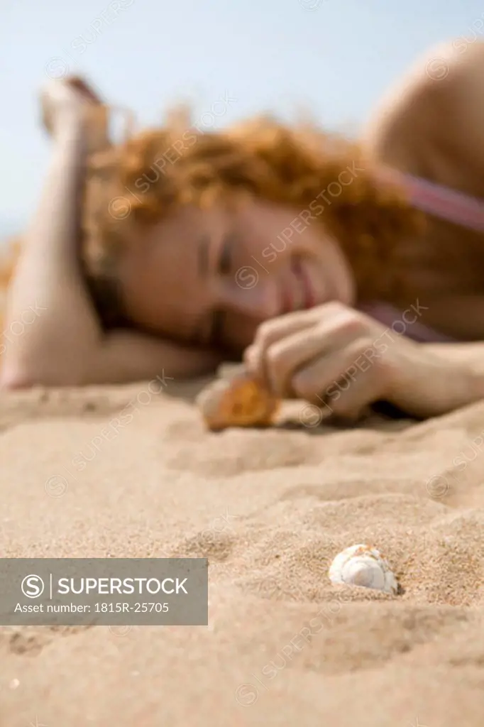 Young woman lying in sand, focus on shell at foreground, close-up