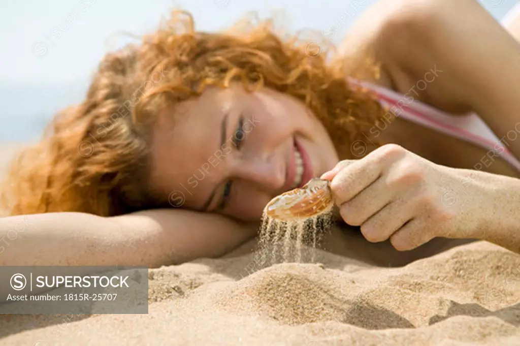 Young woman lying in sand, playing with shell, close-up