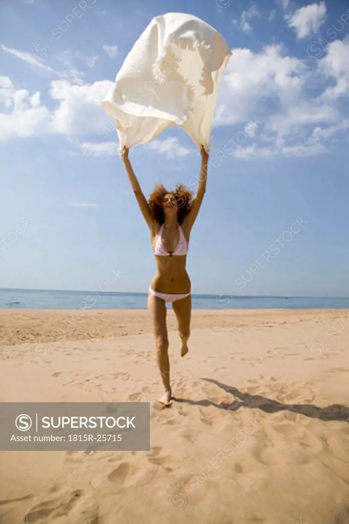 Young woman running on beach, holding bath towel