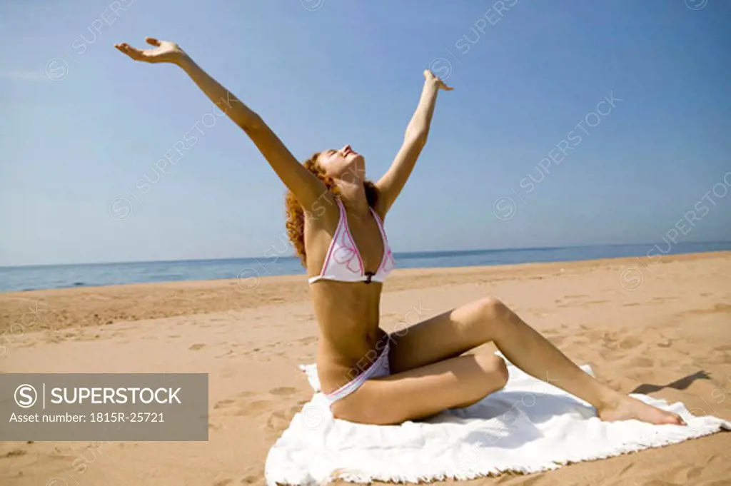 Young woman sitting on bath towel, stretching arms