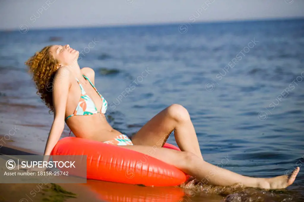 Young woman sitting on inflatable ring on beach, eyes closed