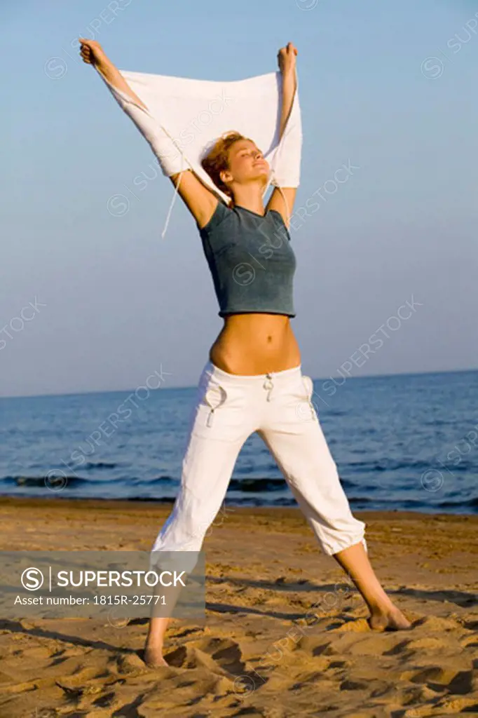 Young woman stretching on beach, legs apart