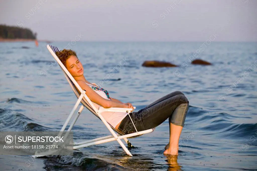 Young woman resting in deck chair on beach, side view