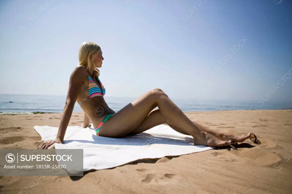 Young woman sitting on beach and looking at view, side view