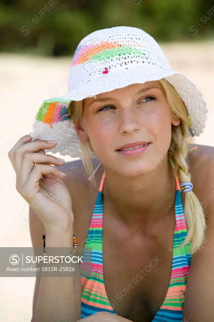 Young woman wearing sun hat on beach, looking away, close-up