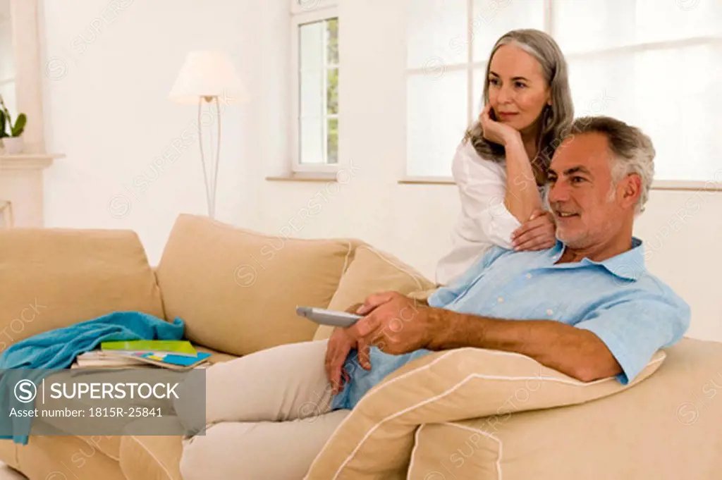 Mature couple in living room, man using remote control
