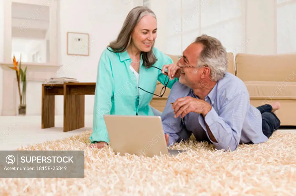 Mature couple lying on carpet with laptop, smiling