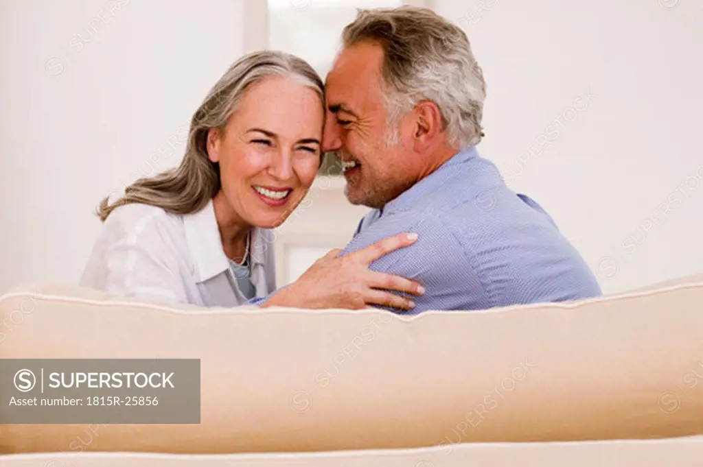 Mature couple embracing on sofa, smiling, close-up