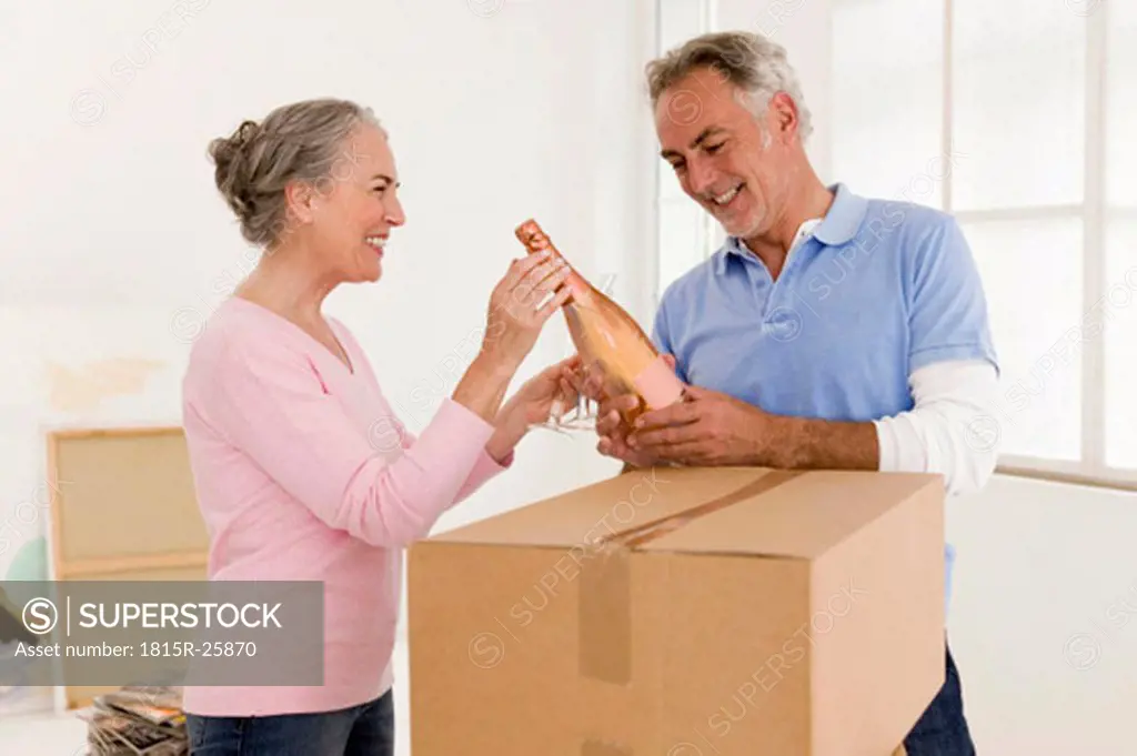Mature couple holding champagne bottle, smiling