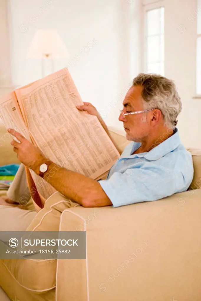 Mature man reading newspaper on sofa, side view, close-up