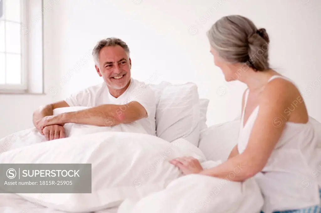 Mature couple sitting on bed, man smiling