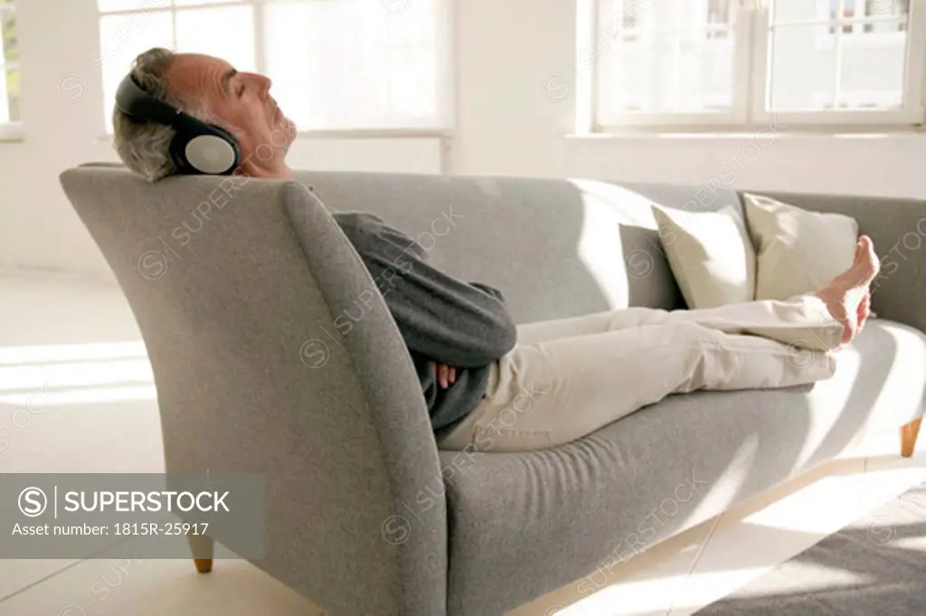 Mature man wearing headphones, sitting on sofa, eyes closed