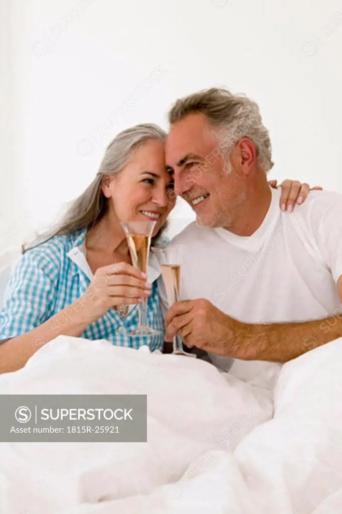 Mature couple on bed toasting champagne, smiling