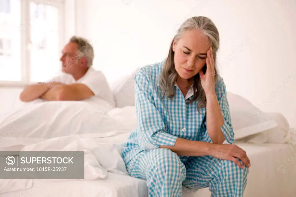 Mature couple sitting on bed (focus on woman in foreground with head in hands)