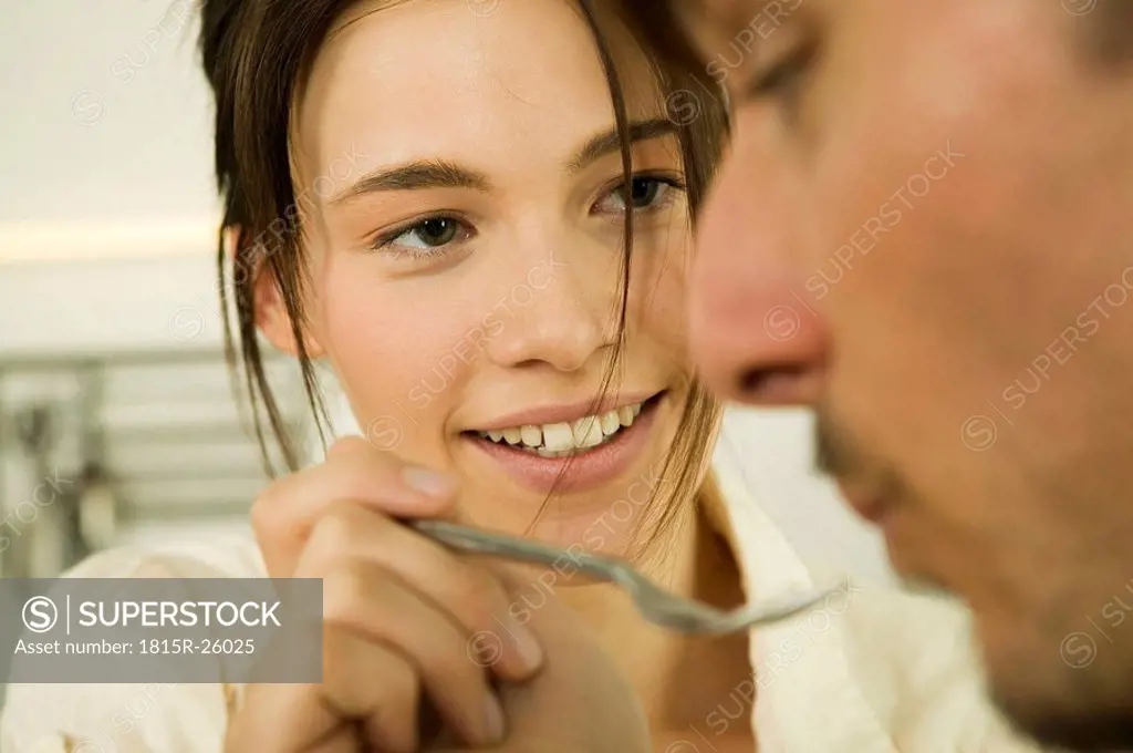 Young couple in kitchen, woman feeding man
