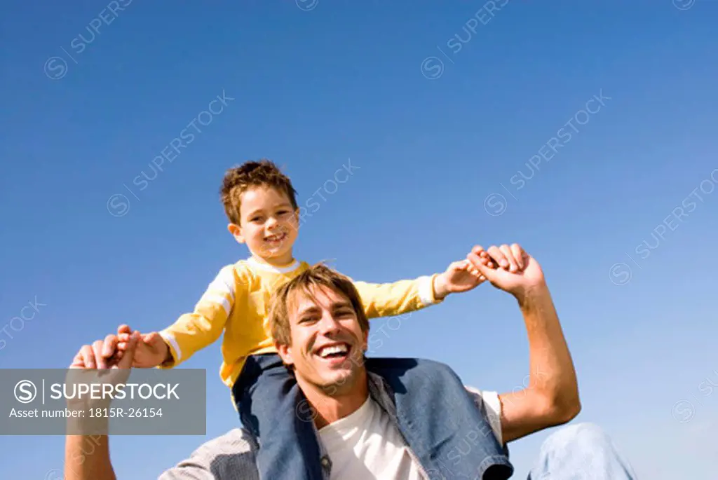 Boy (4-7) sitting on fathers shoulders, smiling, portrait