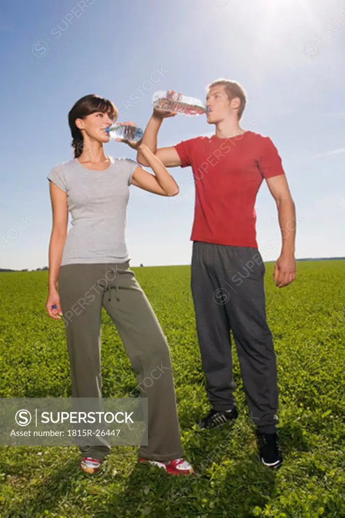 Young couple standing and drinking from water bottle