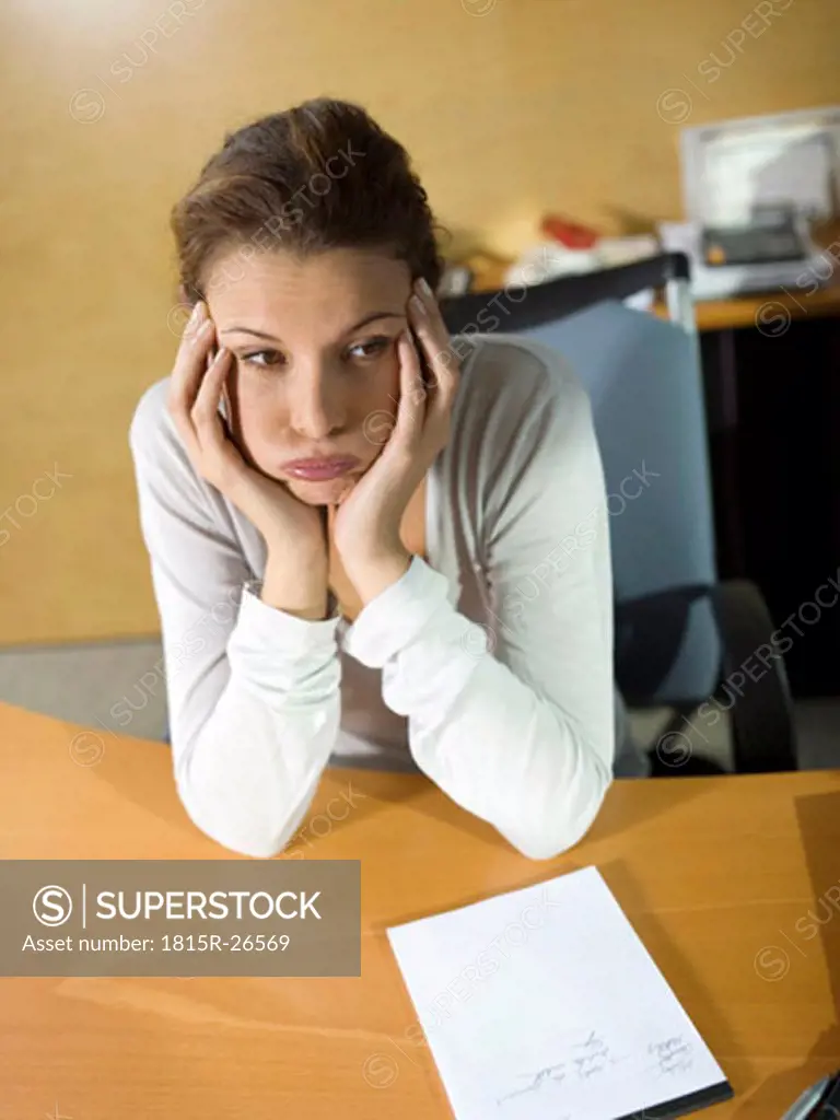 Tired woman sitting at desk, head in hands, close-up