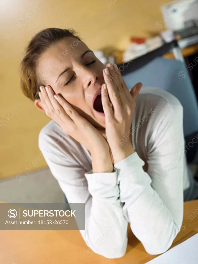 Tired woman sitting at desk, yawning, close-up