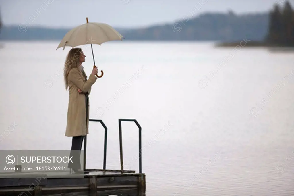 usinesswoman standing on jetty, holding umbrella