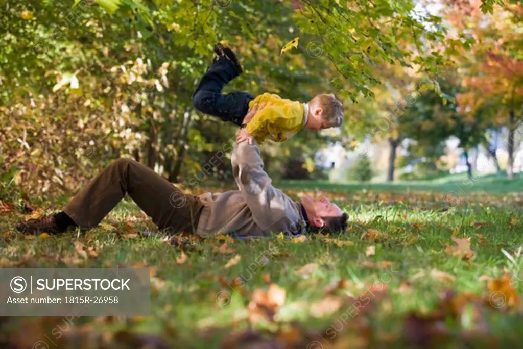 Father lying in meadow, lifting son 6-9