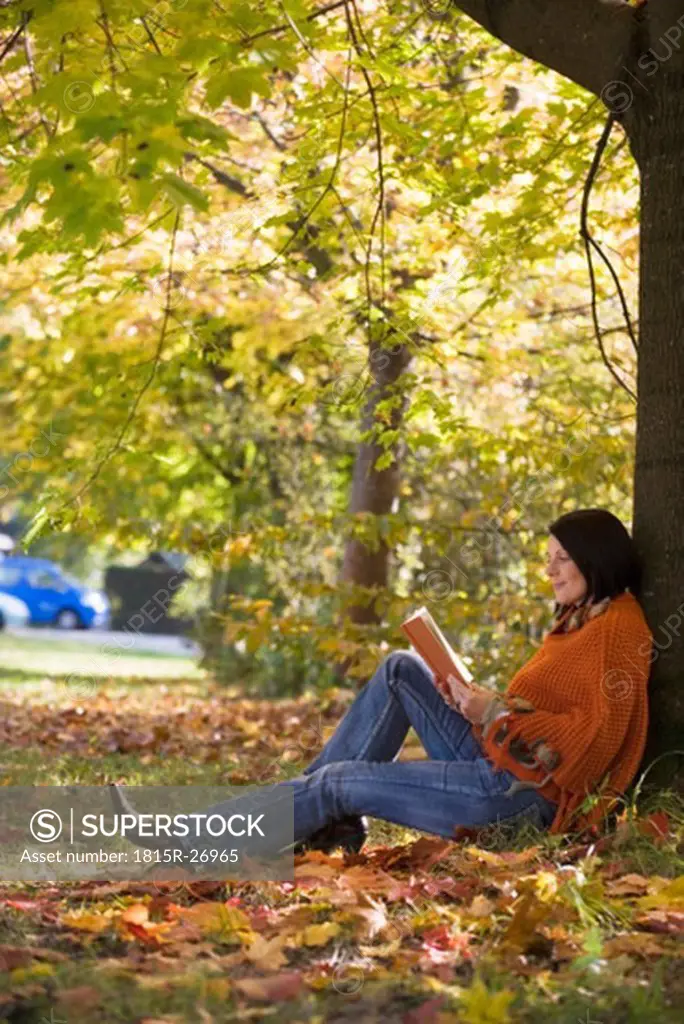 Woman sitting on tree, reading, side view