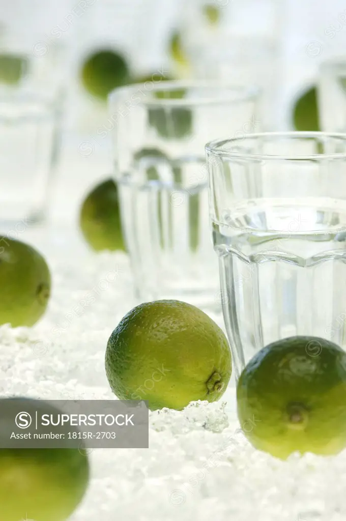 Lime fruits and water glass on crushed ice, close-up