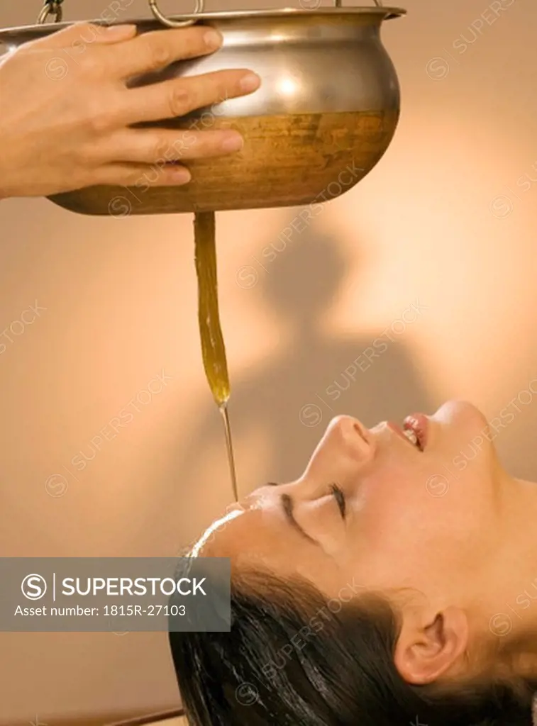 Young woman in spa with oil being poured on forehead, eyes closed