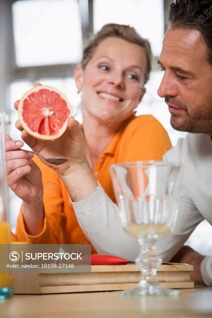 Mature couple eating grapefruit in kitchen, woman smiling