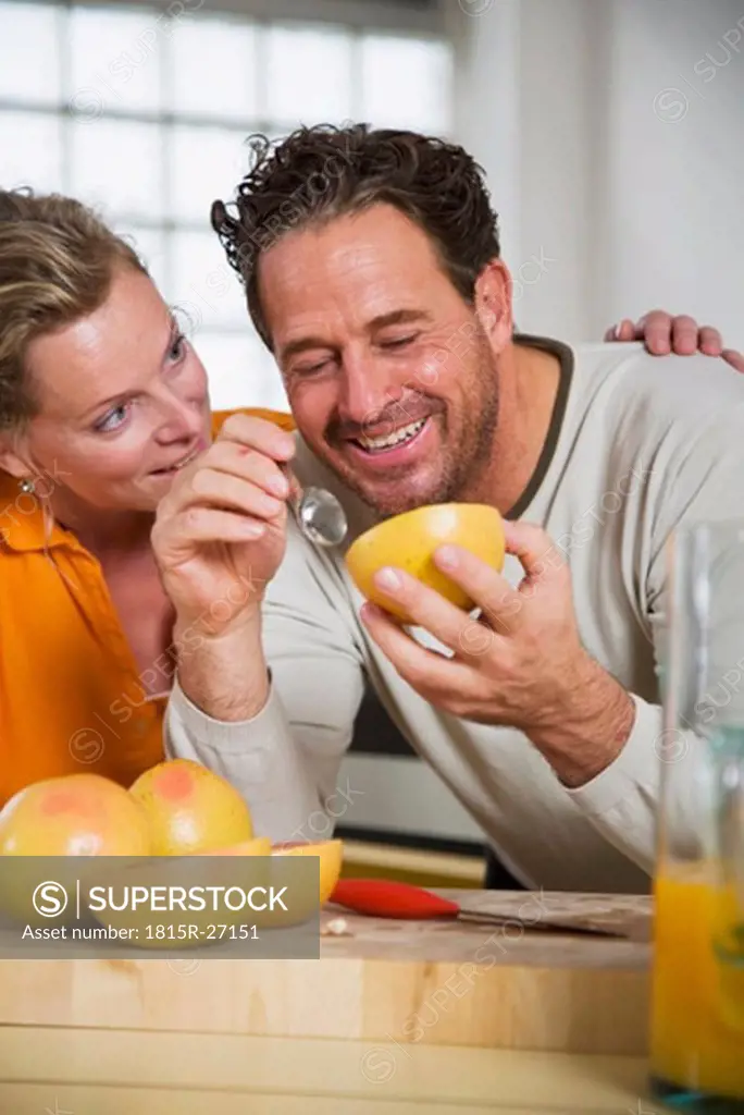 Mature couple eating grapefruit in kitchen, smiling, close-up