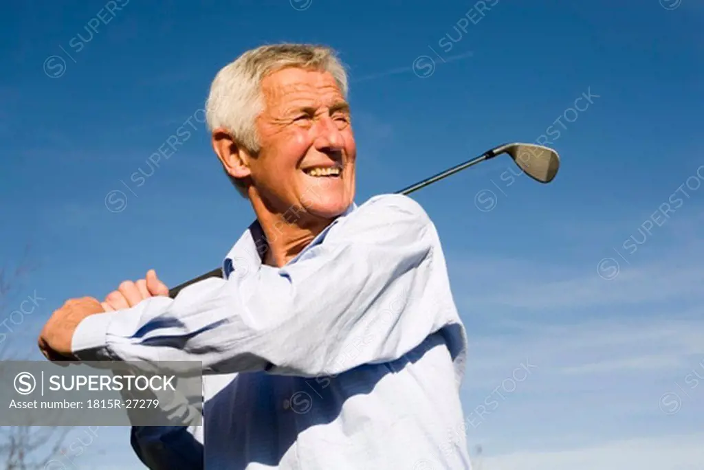 Senior man swinging golf club, smiling, close-up