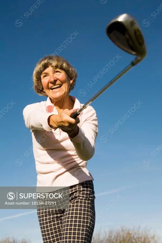 Germany, Bavaria, Ammersee, Senior woman swinging golf club, smiling, low angle view