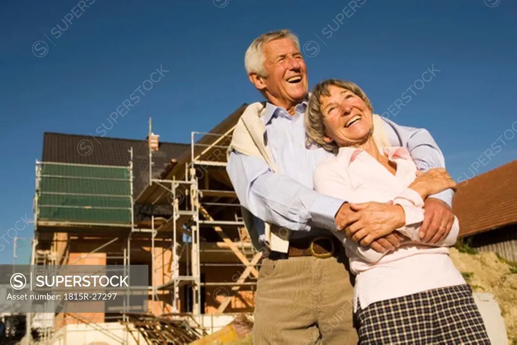 Senior couple embracing in front of construction site, laughing, low angle view
