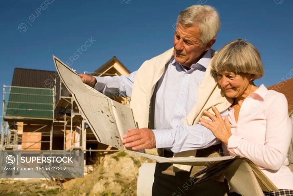 Senior couple holding plan in front of partially built house