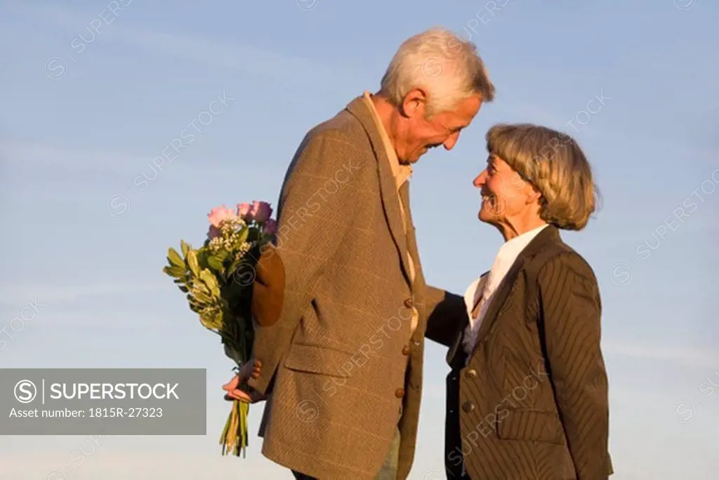 Senior couple, man hiding bouquet, smiling, side view