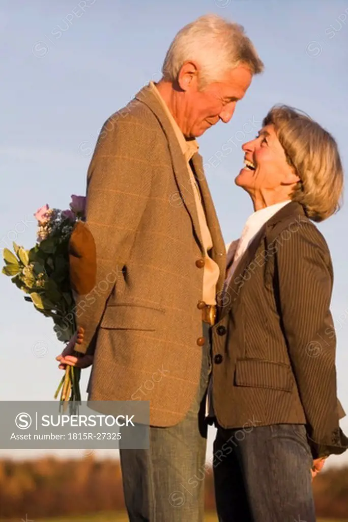 Senior couple, man hiding bouquet, side view