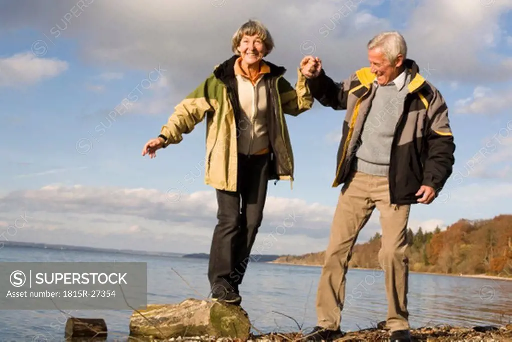 Senior couple hand in hand, woman standing on tree trunk