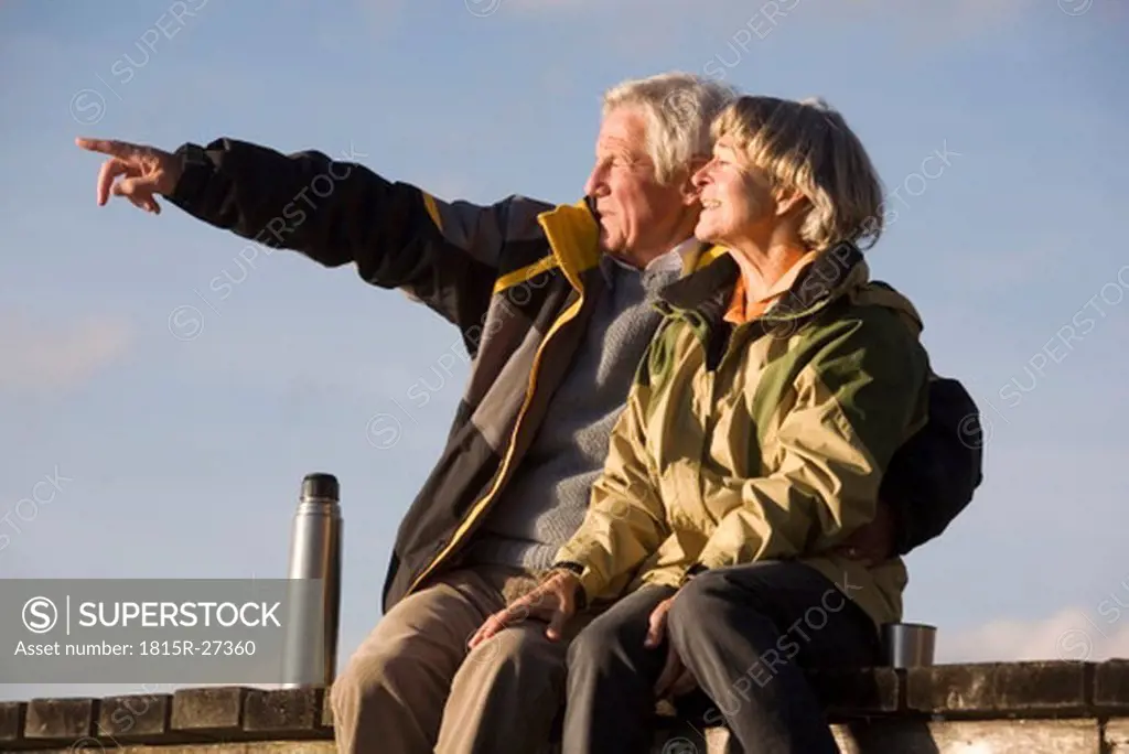 Senior couple sitting on jetty, man pointing