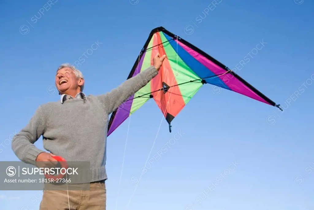 Senior man flying kite, smiling, low angle view