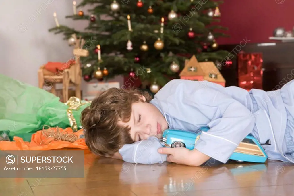Boy sleeping under Christmas tree, holding toy car