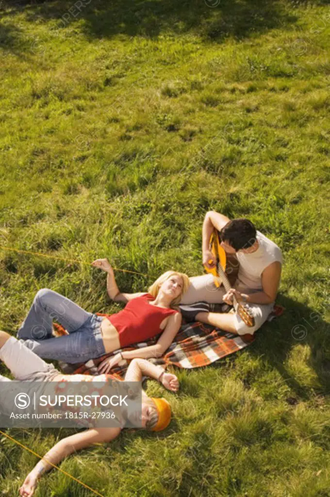 Three young people having picnic, man playing guitar