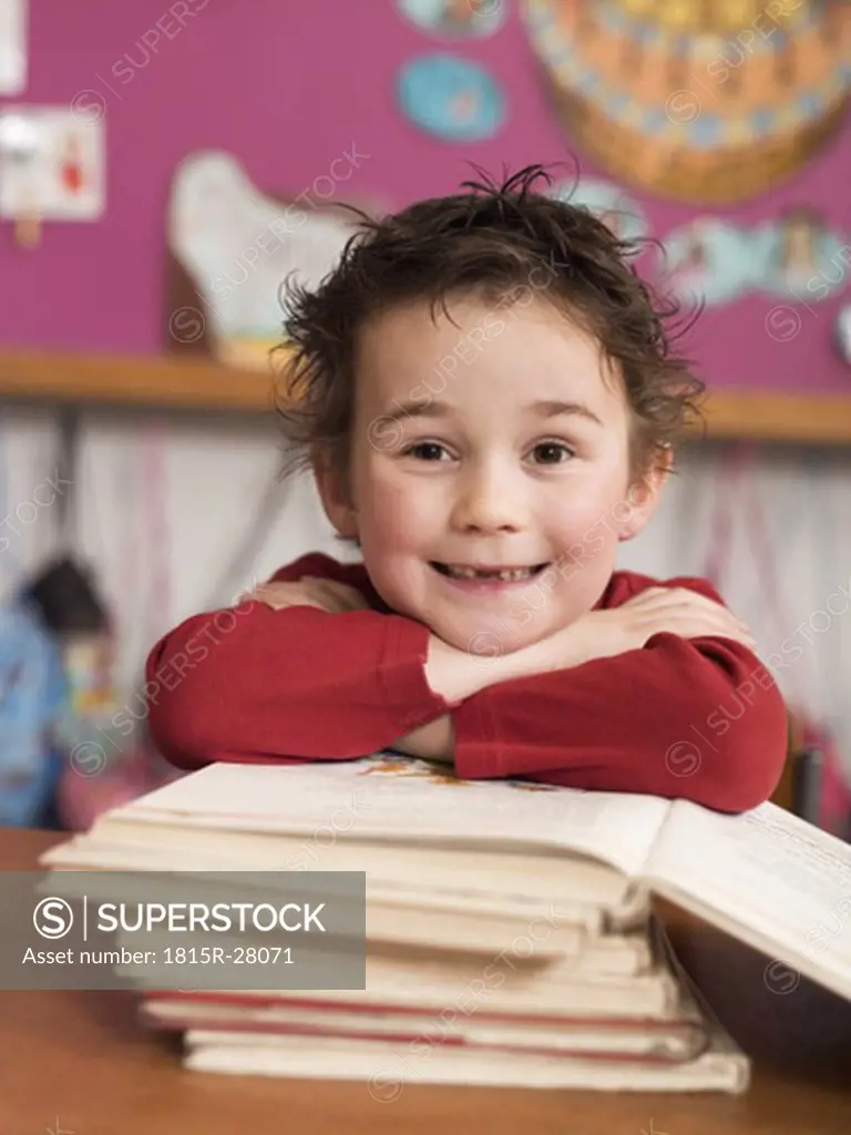 Boy sitting at school desk, leaning on stack of books